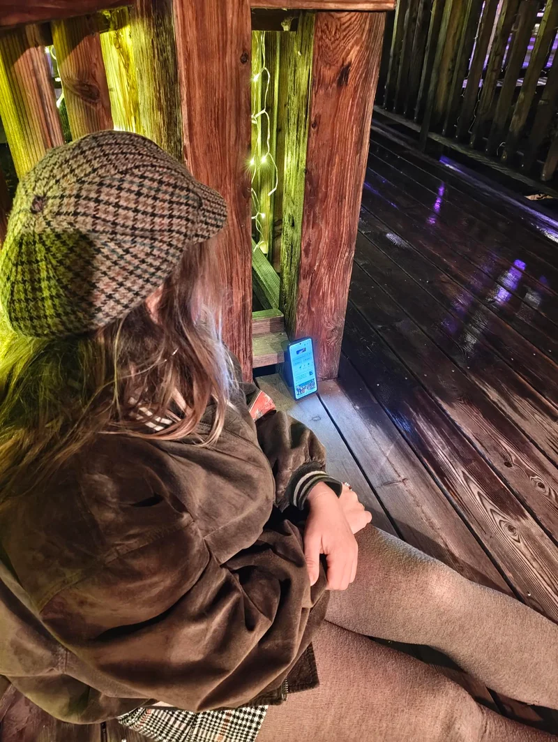 Person mit Mütze sitzt auf einer Holzterrasse neben einem Smartphone